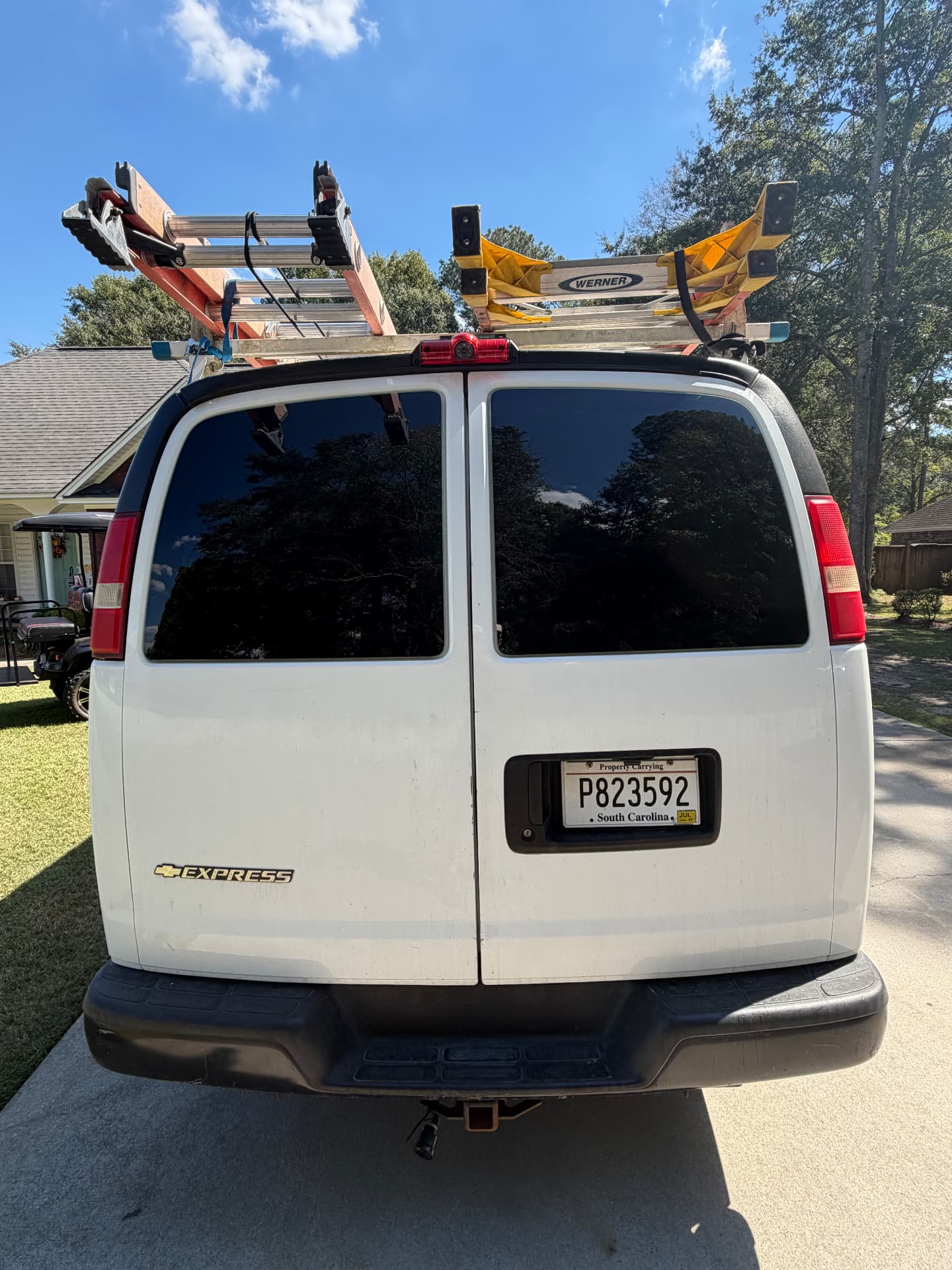 Rear view of a white Chevrolet work van with tinted rear windows and ladders on its roof