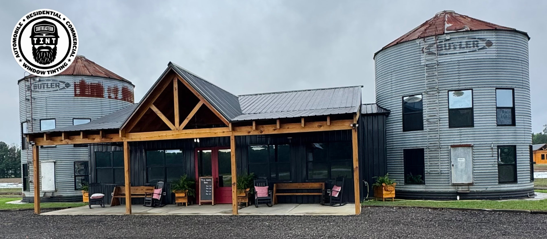 Silo-style building with dark windows and a timber-front porch, with Southeastern Tint logo